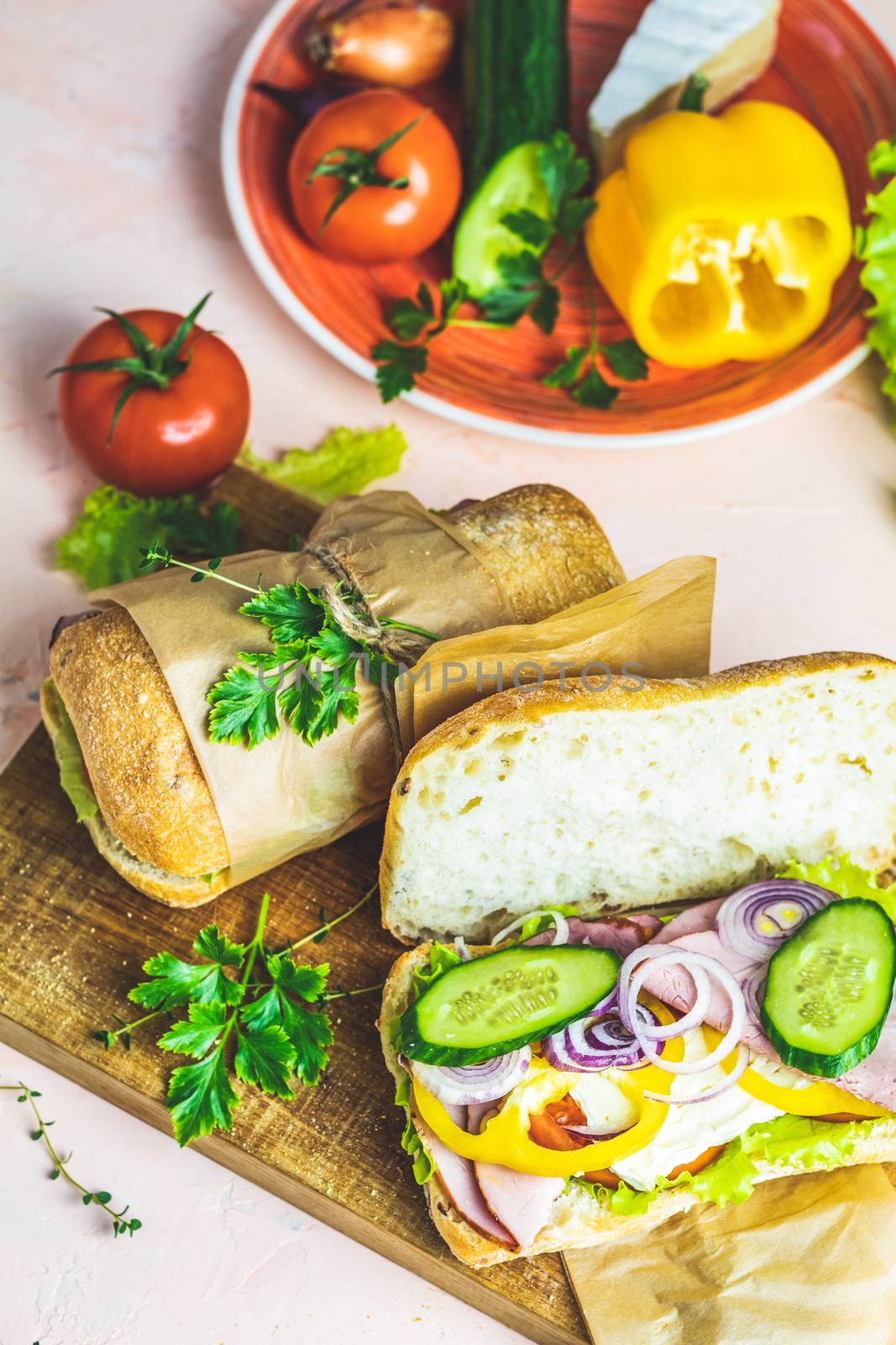 Italian porchetta sandwich. Ciabatta sandwich with ham, tomato, cheese, pepper, onion and salad on wooden cutting board with ingredients.