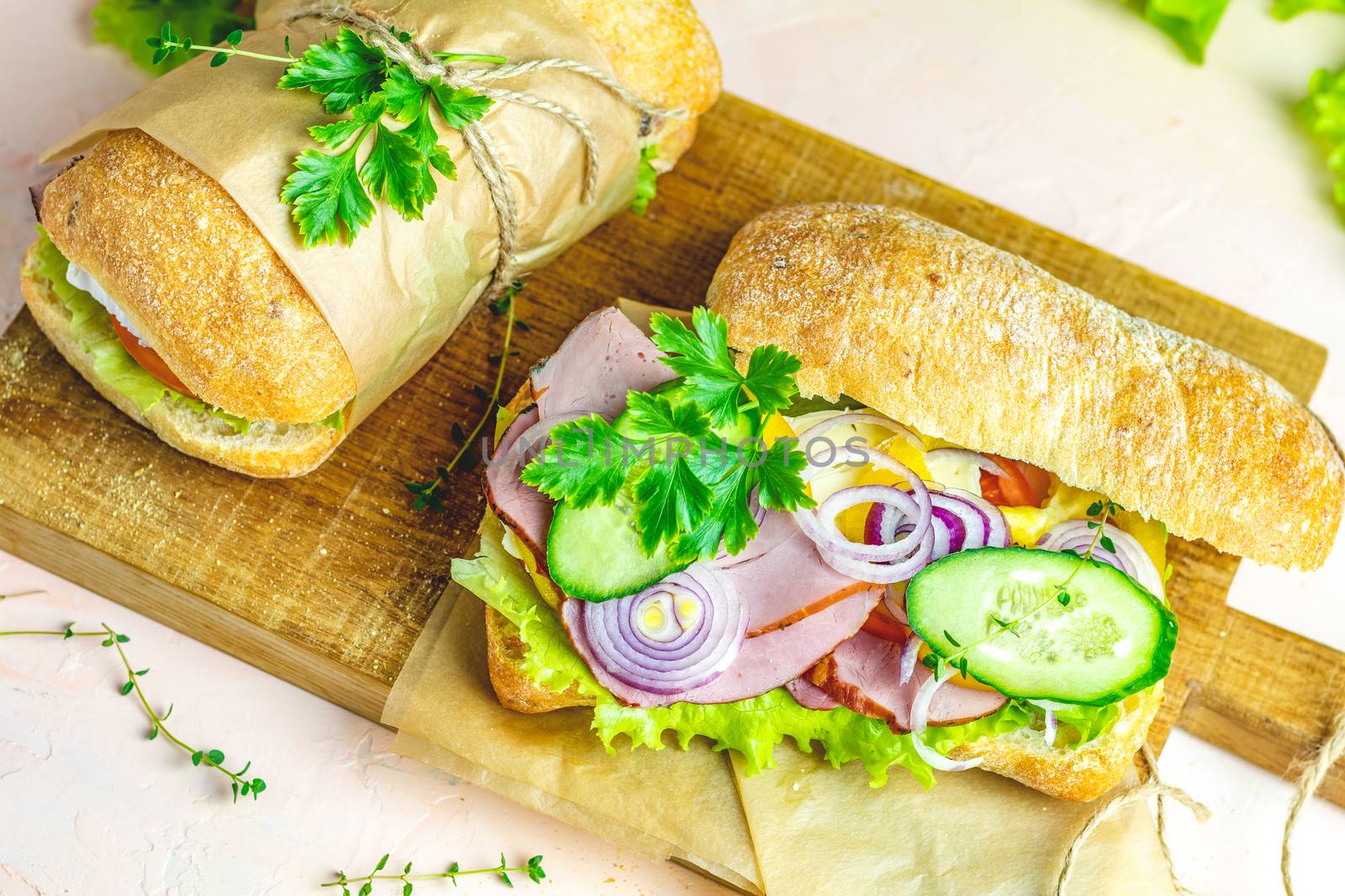 Italian porchetta sandwich. Ciabatta sandwich with ham, tomato, cheese, pepper, onion and salad on wooden cutting board with ingredients.