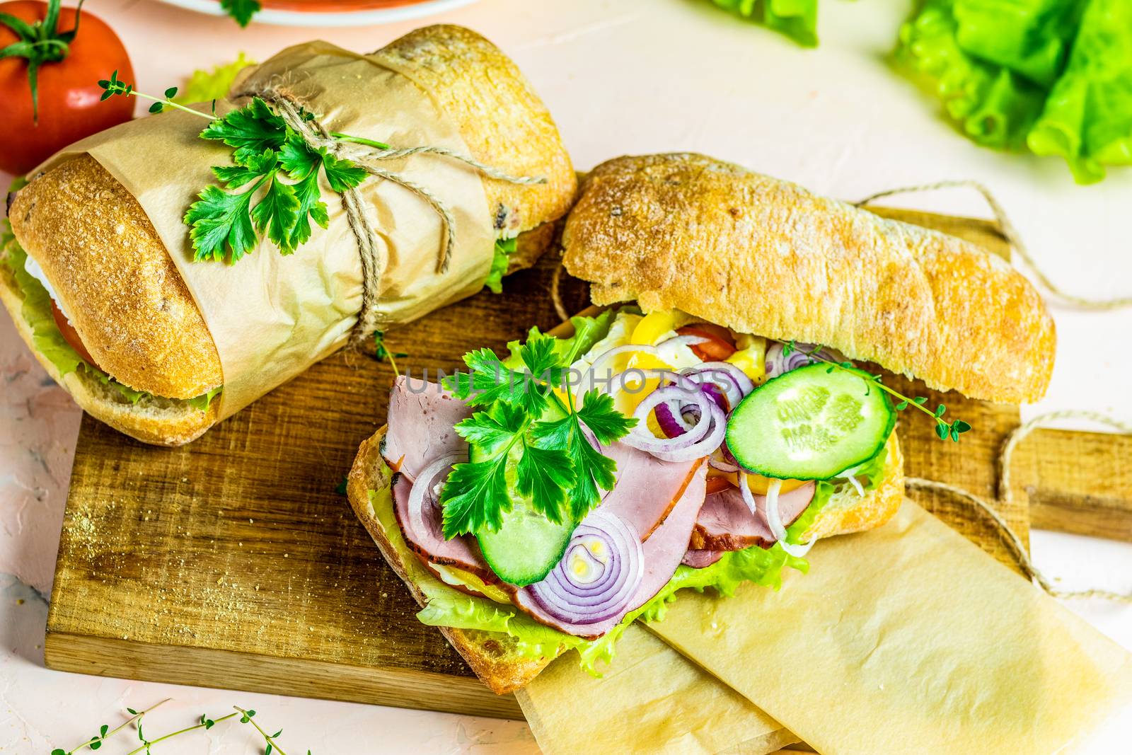 Italian porchetta sandwich. Ciabatta sandwich with ham, tomato, cheese, pepper, onion and salad on wooden cutting board with ingredients.