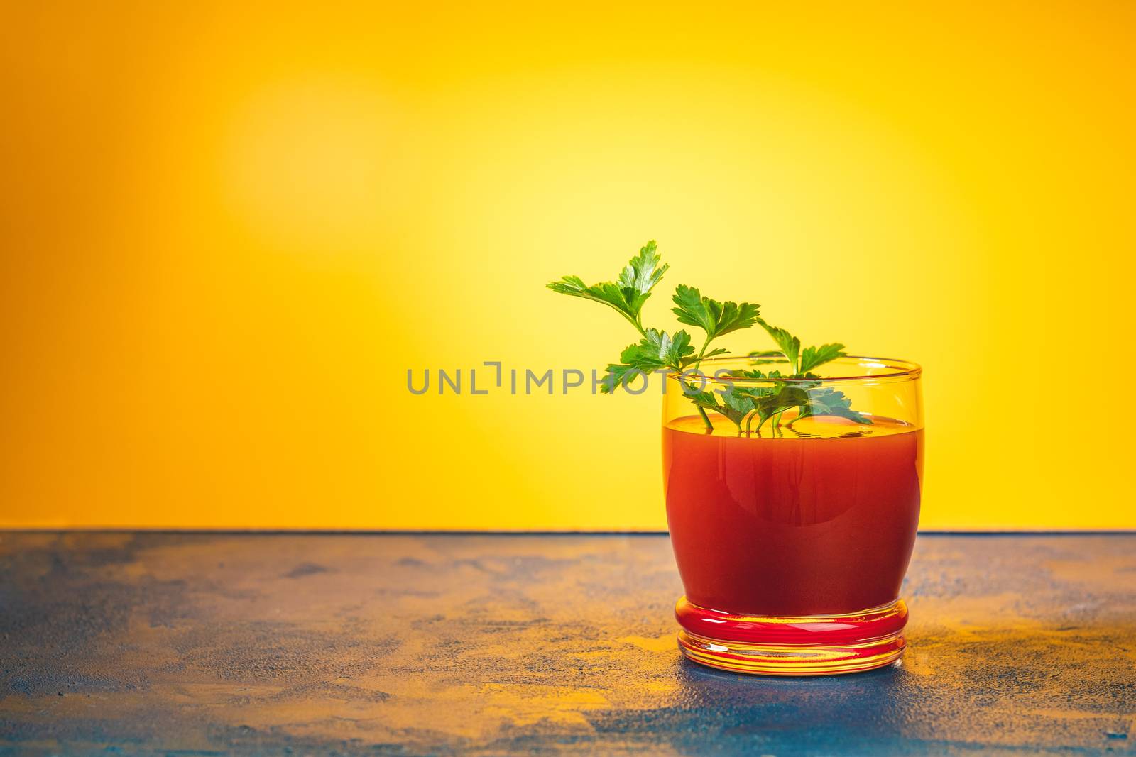 Delicious tomato bloody mary cocktail on dark blue concrete table with spot light. Yellow background.