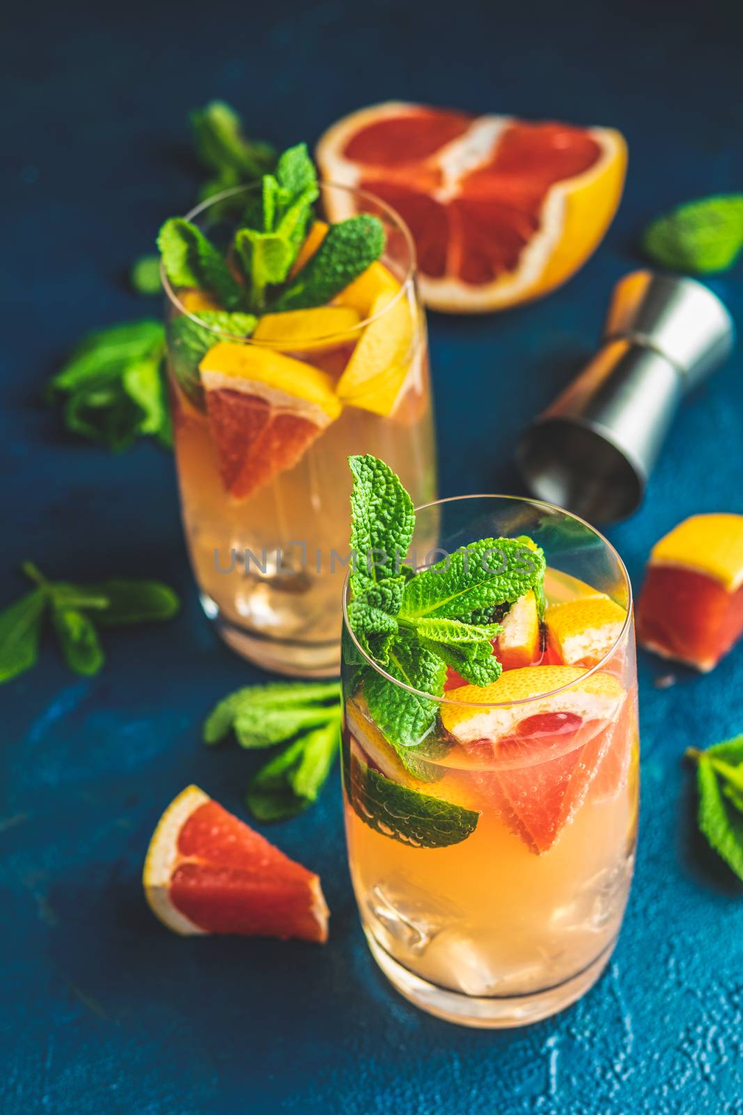 Grapefruit and mint gin tonic cocktail, refreshing drink with ice. Cold summer citrus refreshing drink cocktail or beverage with ice on dark blue concrete surface close up.