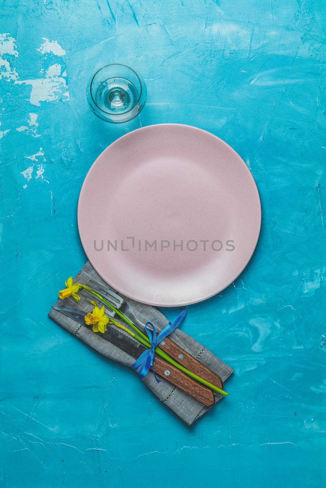 Empty pink plate and cutlery with daffodils on a napkin. Top view, green concrete surface background, copy space for you text