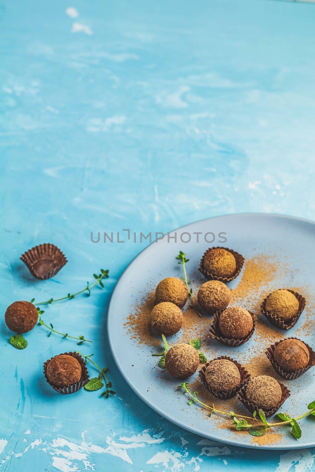 Cocoa balls, handmade chocolate balls cakes in a blue tray, sprinkled with cocoa powder, fresh mint and thyme on dark blue concrete surface background. Close up, copy space, shallow depth of the field