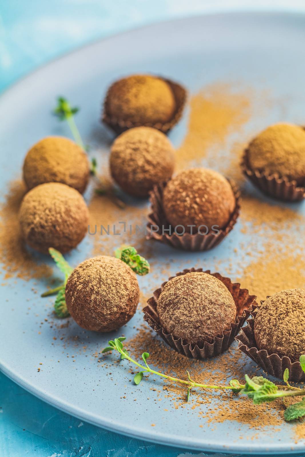 Cocoa balls, handmade chocolate balls cakes in a blue tray, sprinkled with cocoa powder, fresh mint and thyme on dark blue concrete surface background. Close up, copy space, shallow depth of the field