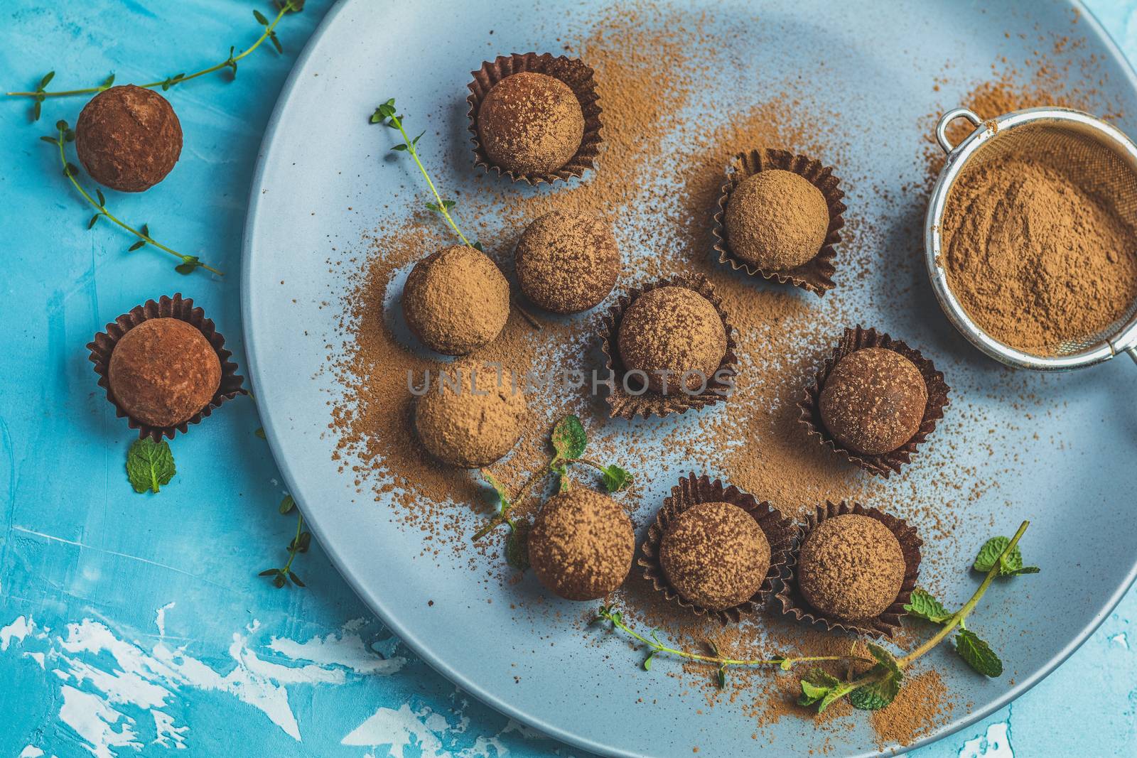Cocoa balls, handmade chocolate balls cakes in a blue tray, sprinkled with cocoa powder, fresh mint and thyme on dark blue concrete surface background. Close up, copy space, shallow depth of the field