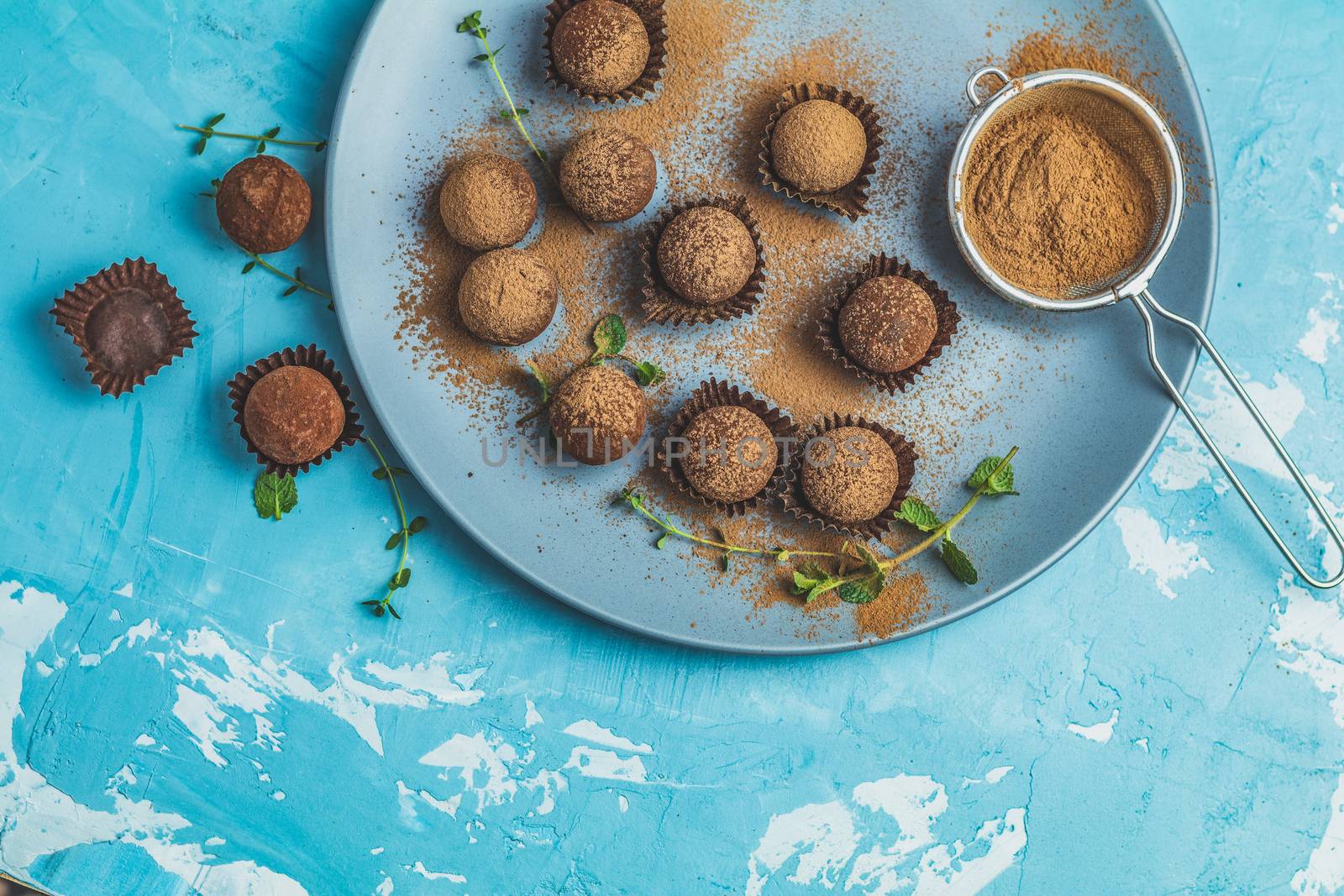 Cocoa balls, handmade chocolate balls cakes in a blue tray, sprinkled with cocoa powder, fresh mint and thyme on dark blue concrete surface background. Close up, copy space, shallow depth of the field