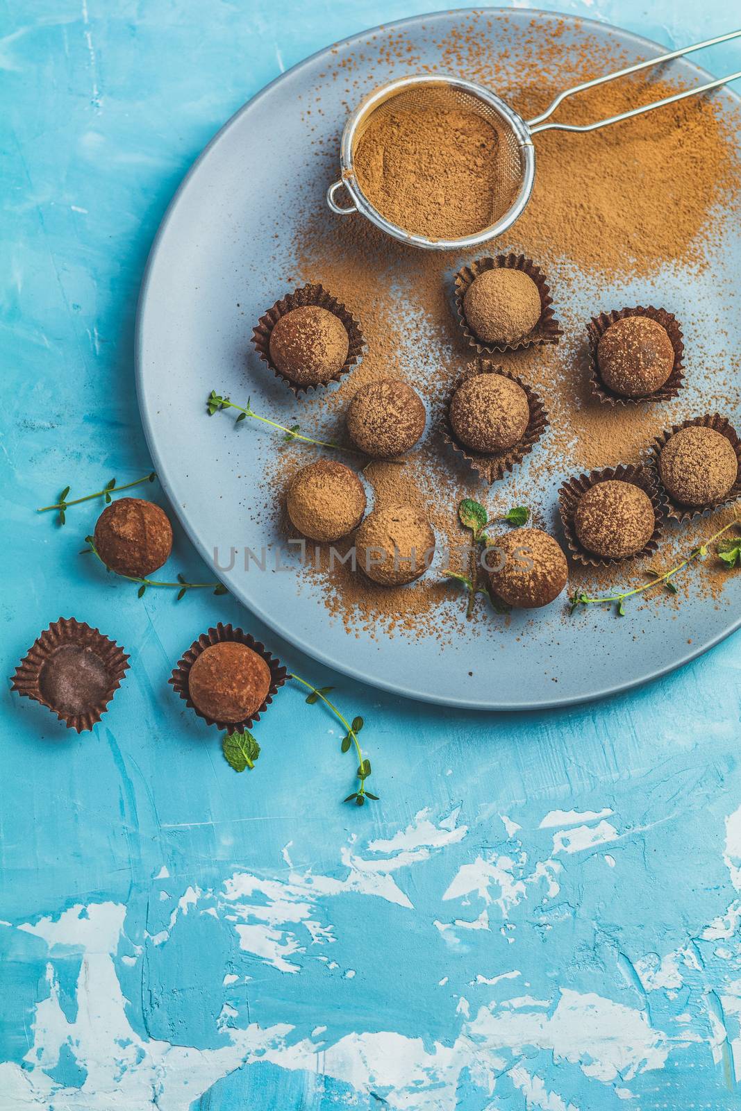 Cocoa balls, handmade chocolate balls cakes in a blue tray, sprinkled with cocoa powder, fresh mint and thyme on dark blue concrete surface background. Close up, copy space, shallow depth of the field