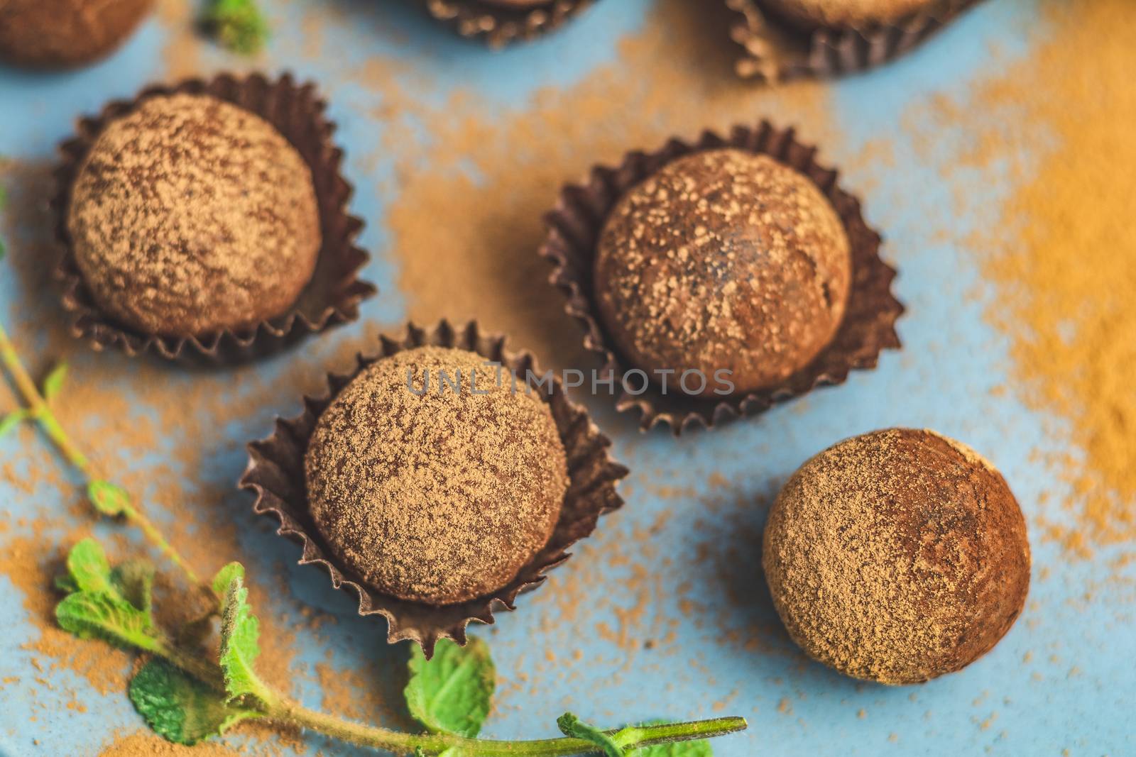 Cocoa balls, handmade chocolate balls cakes in a blue tray, sprinkled with cocoa powder, fresh mint and thyme on dark blue concrete surface background. Close up, copy space, shallow depth of the field