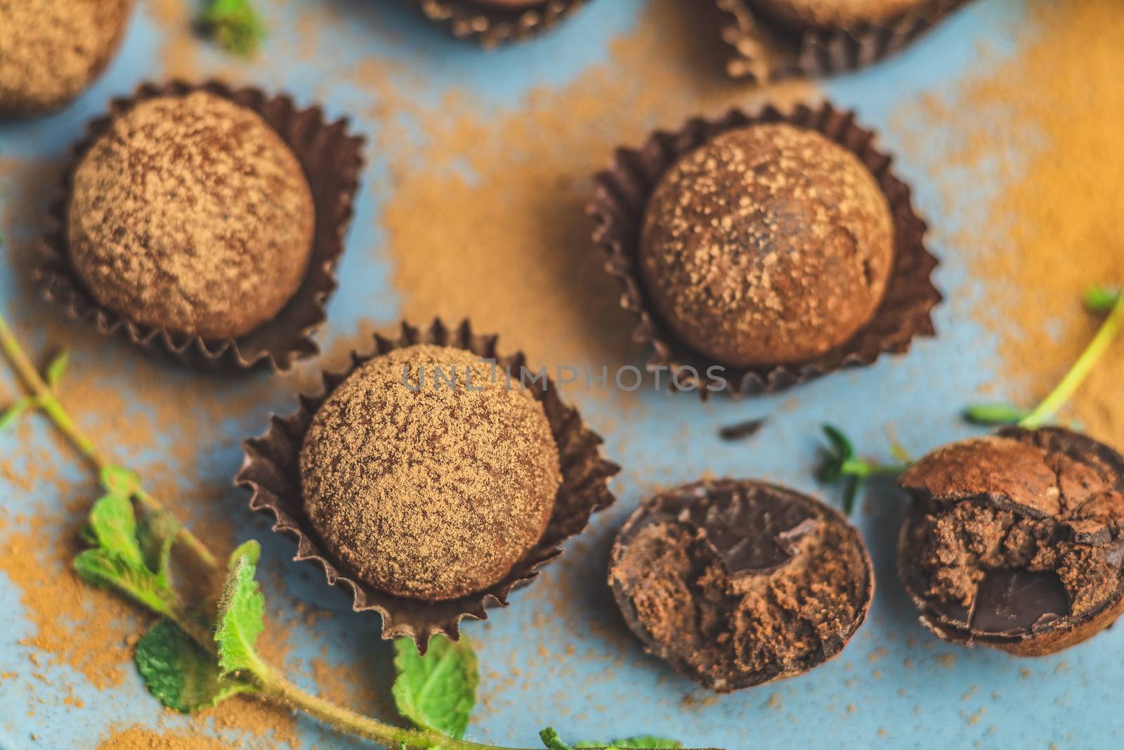 Cocoa balls, handmade chocolate balls cakes in a blue tray, sprinkled with cocoa powder, fresh mint and thyme on dark blue concrete surface background. Close up, copy space, shallow depth of the field