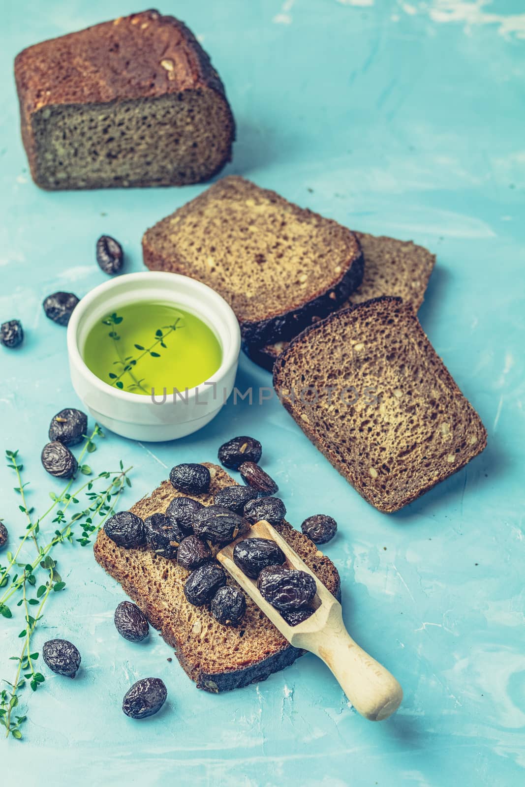 Traditional greek italian appetizer dried black olives with bread and olive oil served on over a blue concrete table surface background