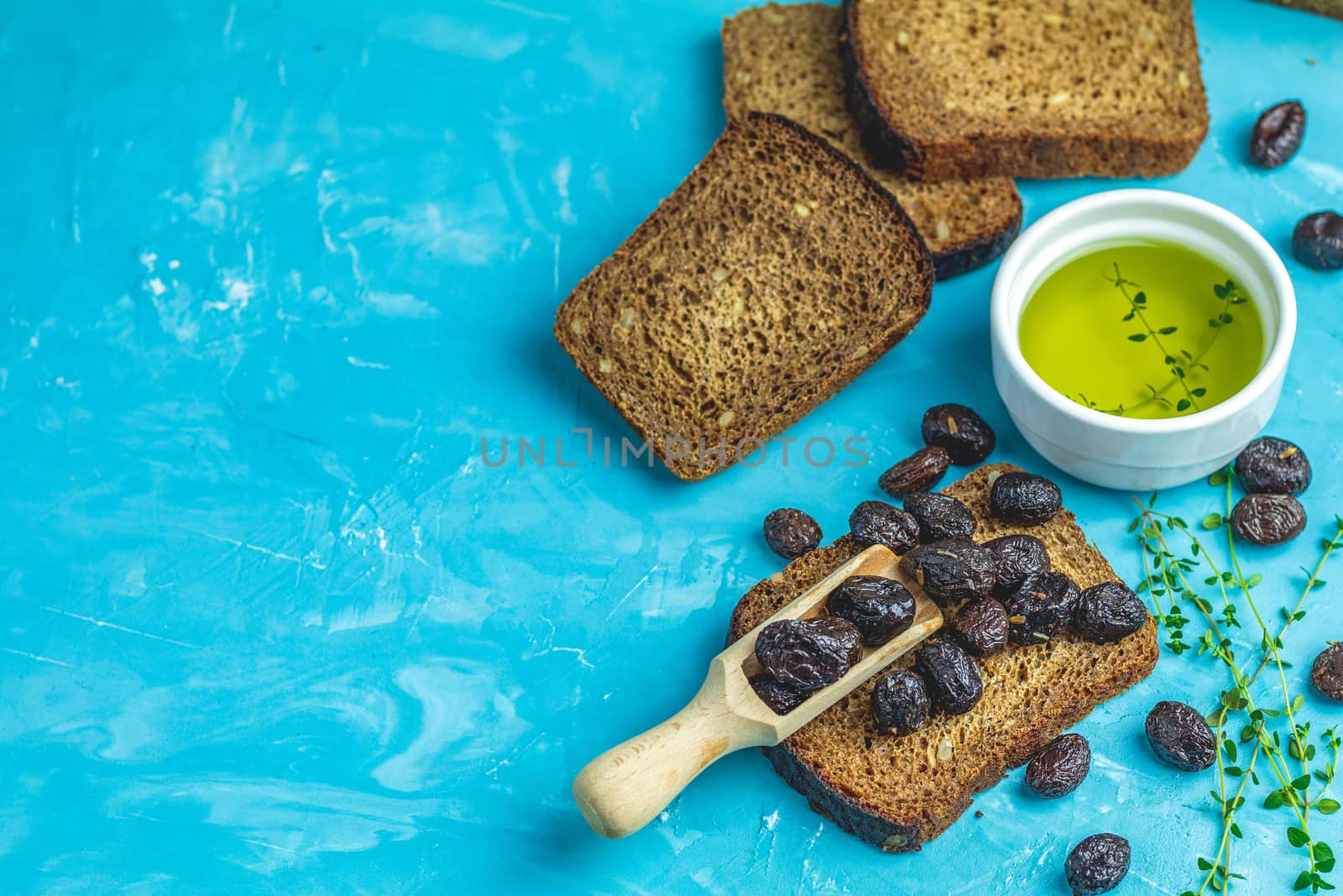 Traditional greek italian appetizer dried black olives with bread and olive oil served on over a blue concrete table surface background