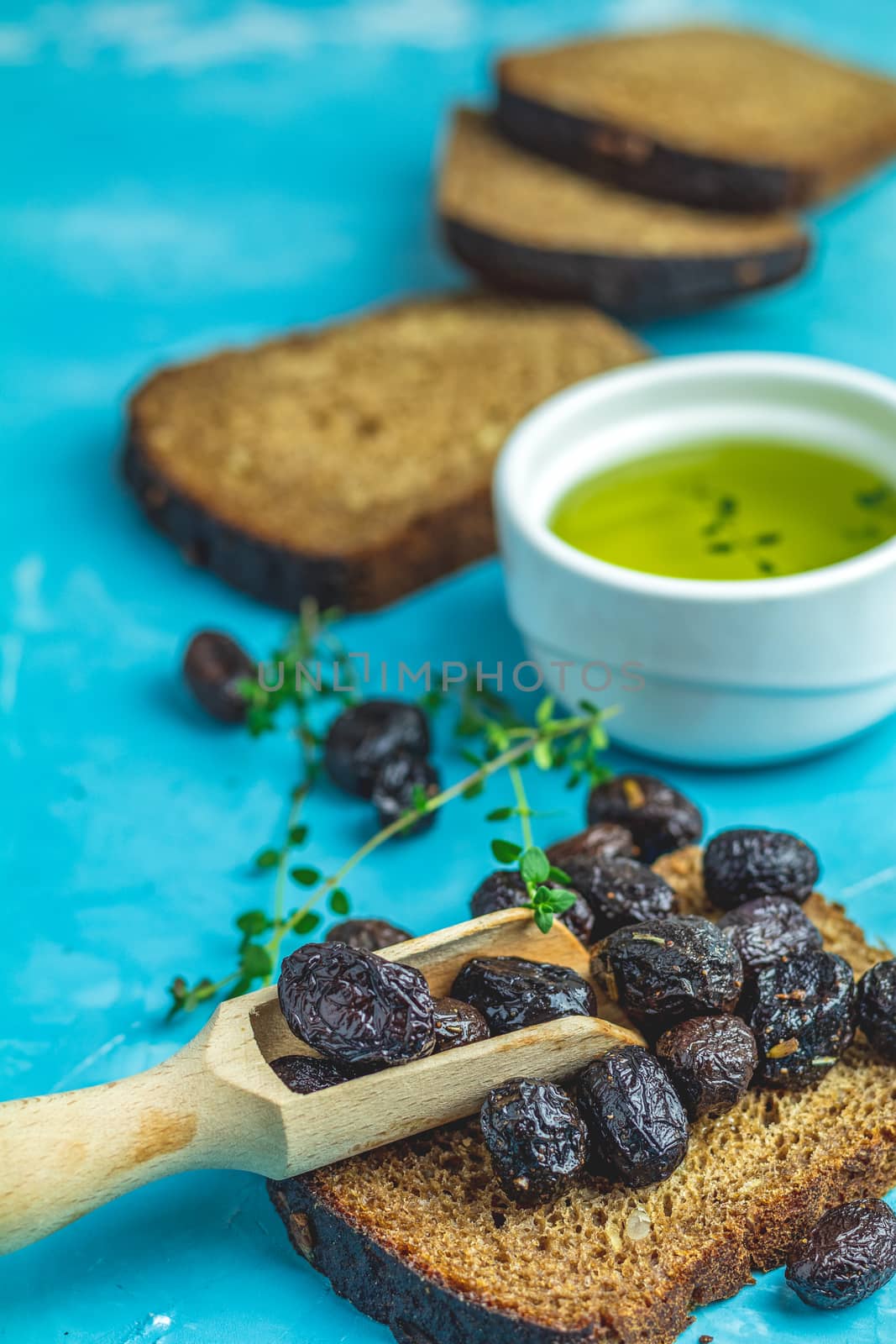Traditional greek italian appetizer dried black olives with bread and olive oil served on over a blue concrete table surface background