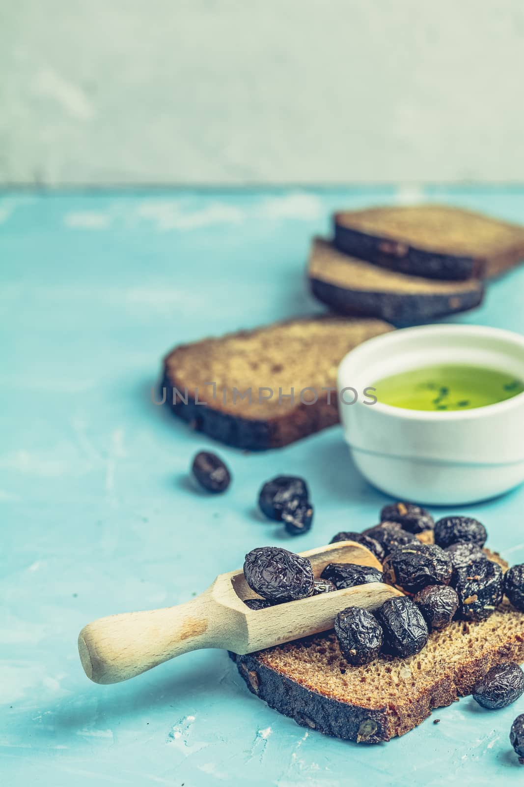 Cream Cheese on a slice of bread topped, bowl of cream cheese, mozzarella, pine nuts and traditional greek italian appetizer dried olives on blue concrete table surface.