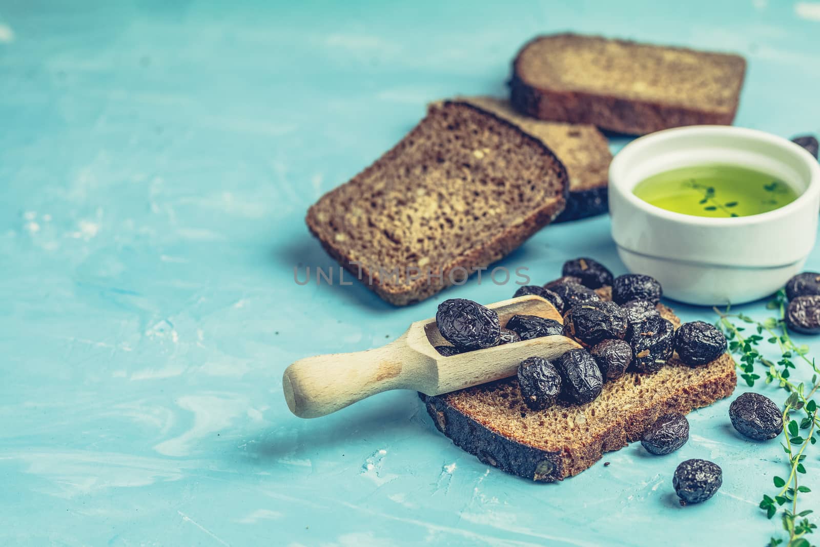 Traditional greek italian appetizer dried black olives with bread and olive oil served on over a blue concrete table surface background