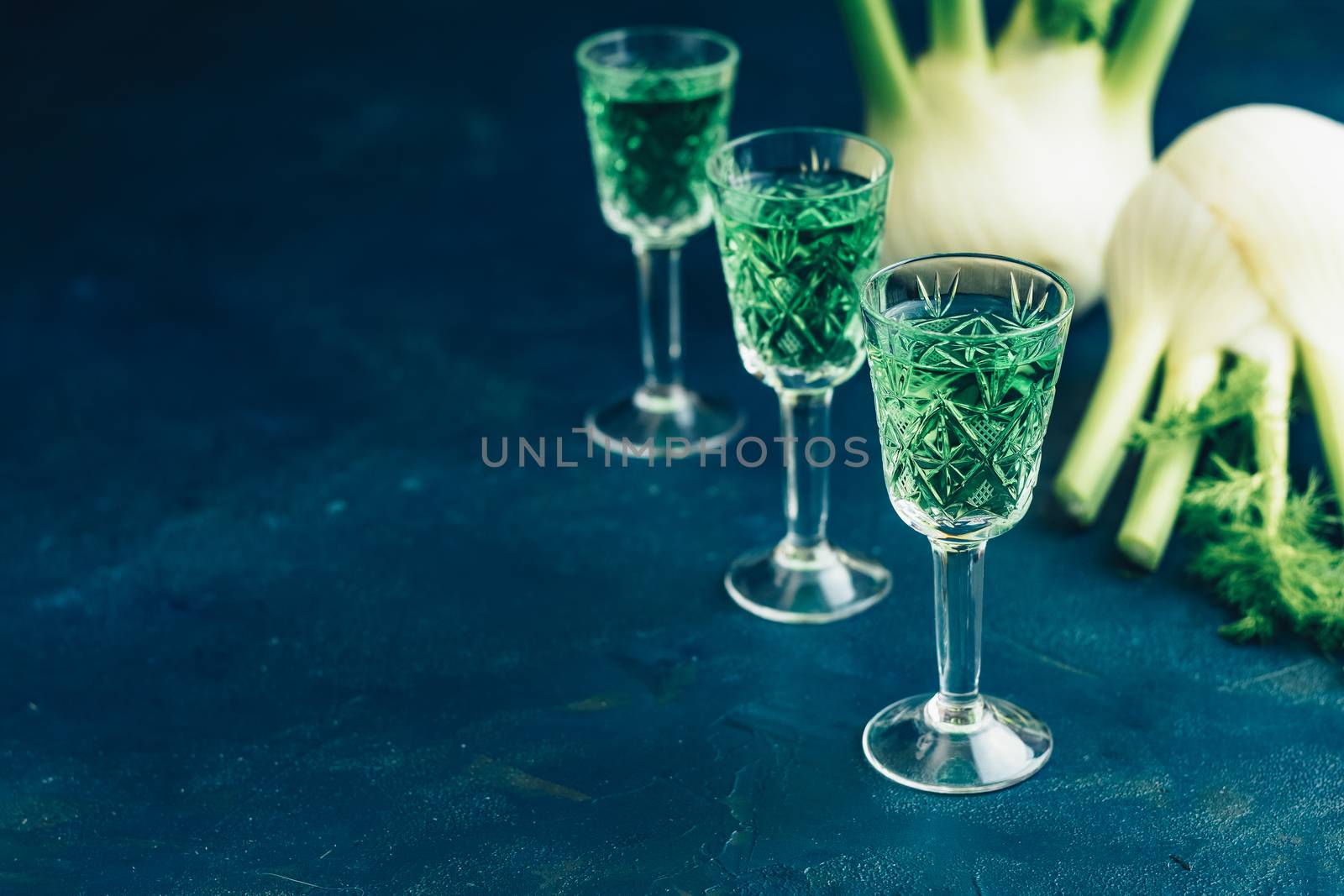 Traditional italian or czech liqueur or bitter with fennel. Three absinthe glass. Dark blue concrete table surface background, copy space for you text.