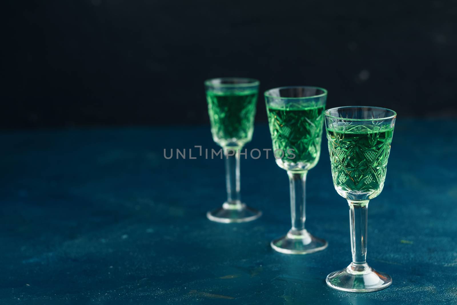 Traditional italian or czech liqueur or bitter with fennel. Three absinthe glass. Dark blue concrete table surface background, copy space for you text.