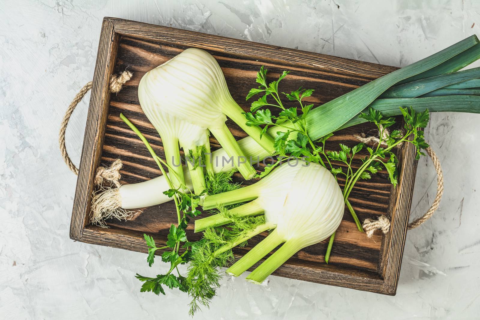 Fresh Florence fennel bulbs or Fennel bulb, leek and parsley in wooden box with dried grass on light gray concrete background. Healthy and benefits of Florence fennel bulbs.