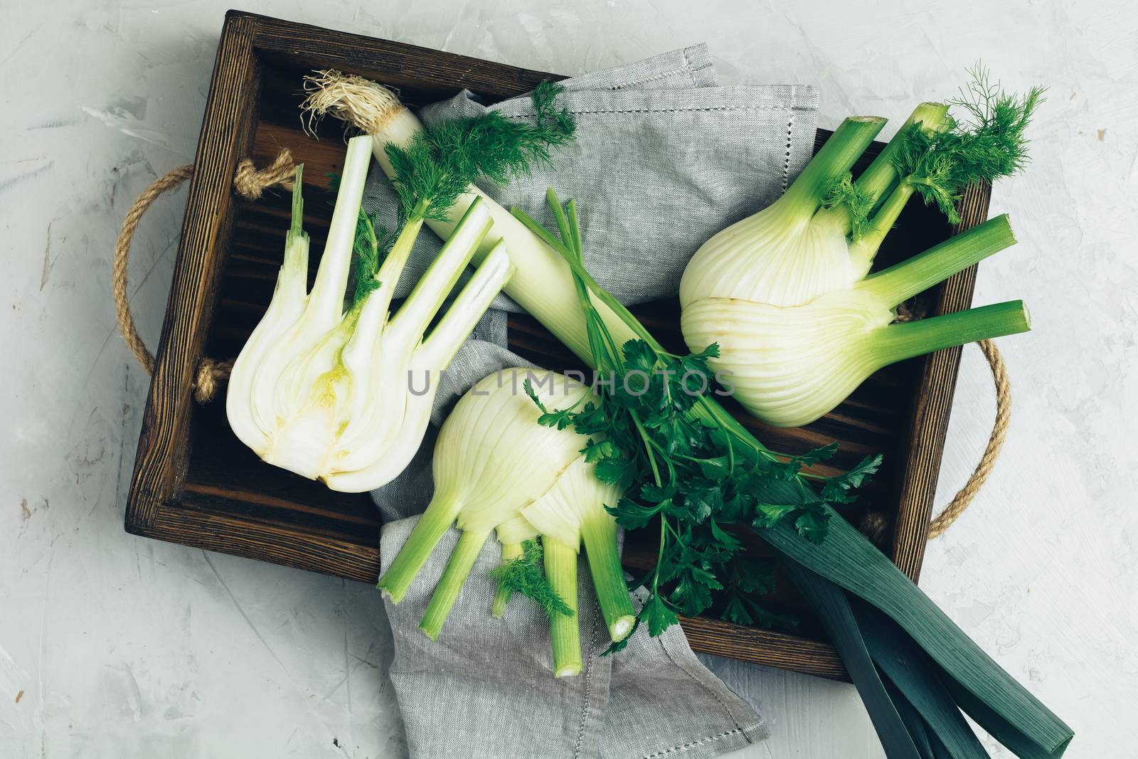 Fresh Florence fennel bulbs or Fennel bulb, leek and parsley in wooden box with dried grass on light gray concrete background. Healthy and benefits of Florence fennel bulbs.