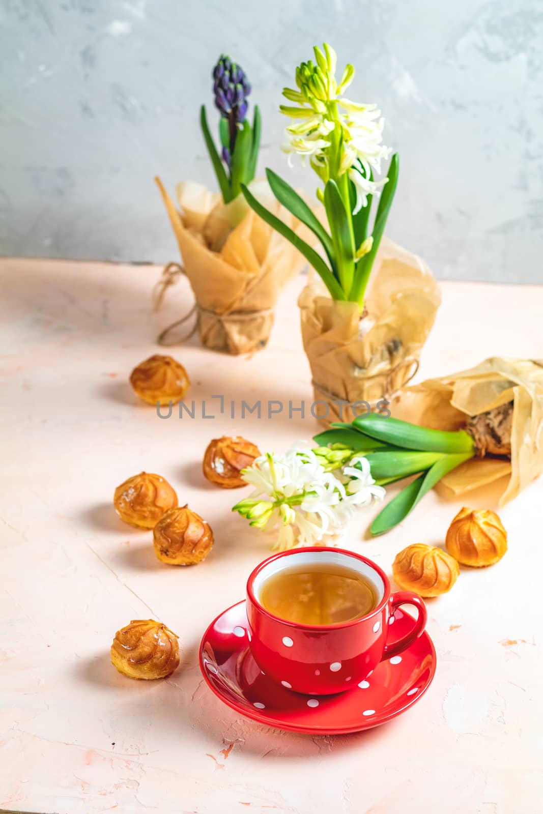 Red in white dotted cup of coffee with milk, delicious profiteroles with cream and white hyacinths on pink concrete surface. Happy Easter, Mothers day, birthday, wedding marriage festive background.