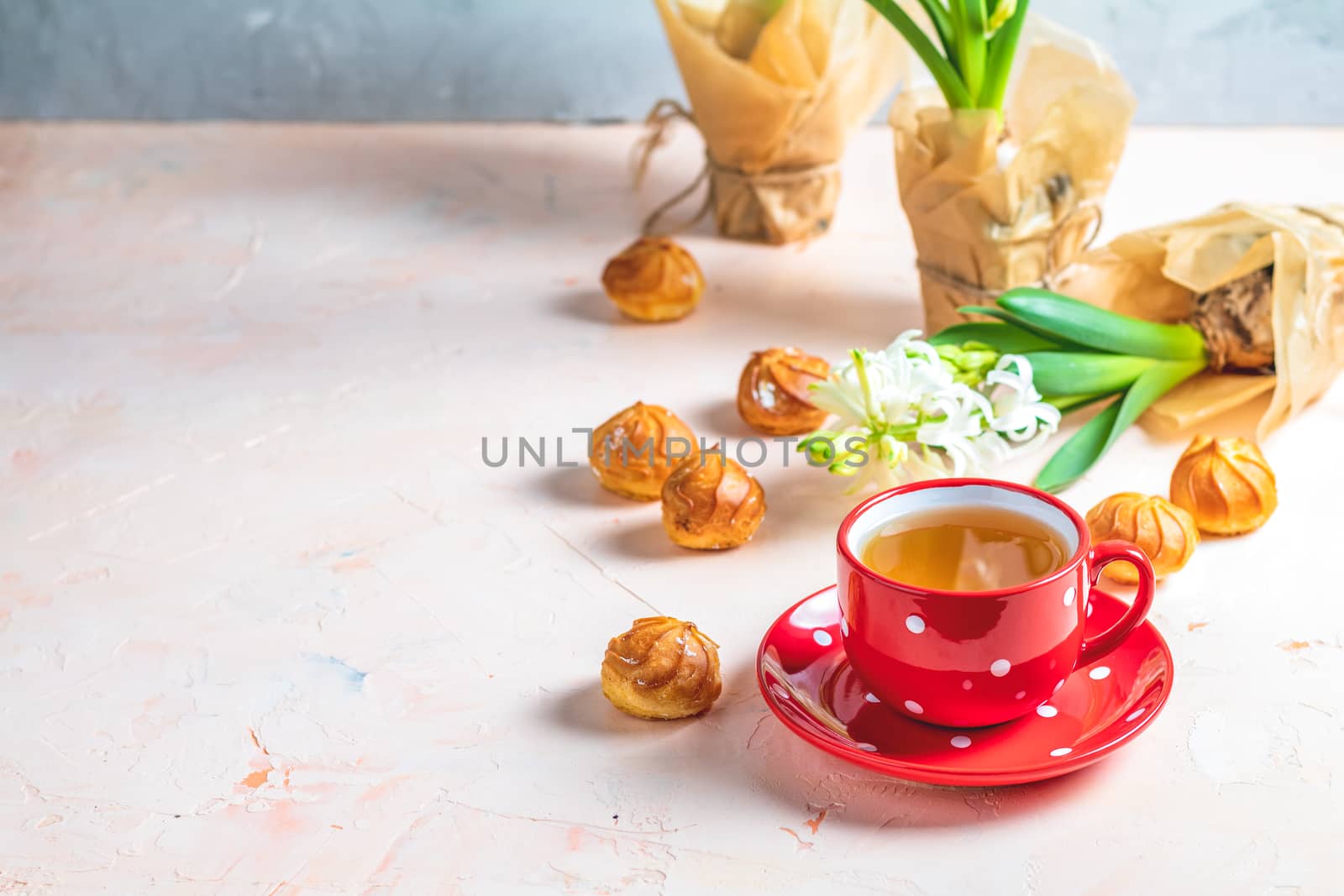 Red in white dotted cup of coffee with milk, delicious profiteroles with cream and white hyacinths on pink concrete surface. Happy Easter, Mothers day, birthday, wedding marriage festive background.