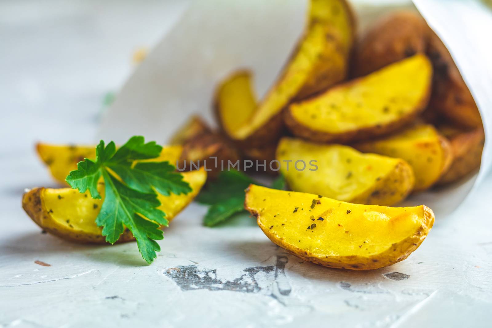 Baked potato wedges on paper with parsley by ArtSvitlyna