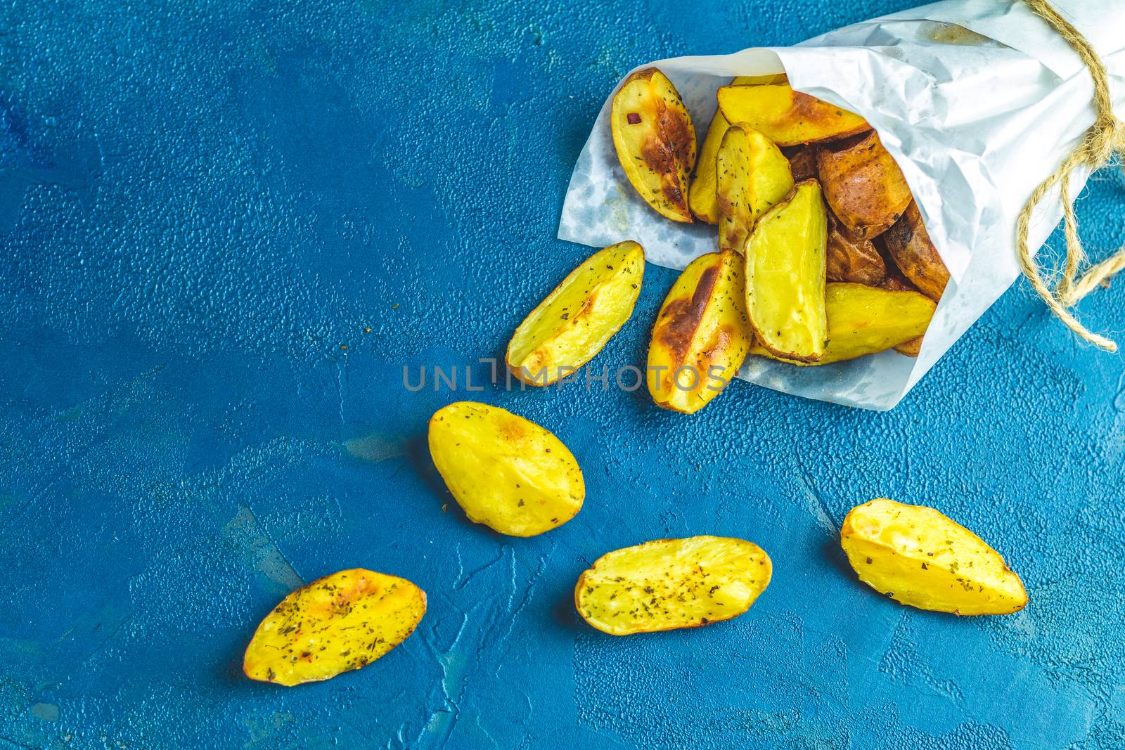 Baked potato wedges on paper with addition sea salt on a dark blue concrete background