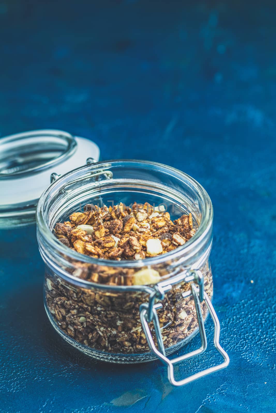 Open glass jar of organic granola on a dark blue concrete table by ArtSvitlyna