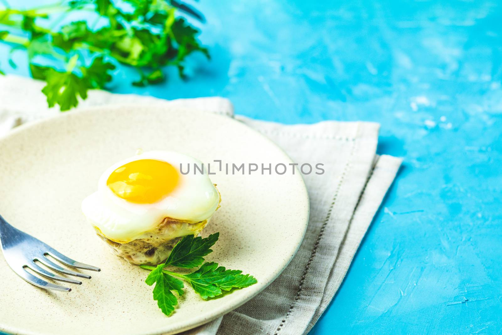 Baked eggs  in light plate and baking molds. Portioned casserole from bacon  and eggs in Italian style. Blue concrete table surface background.