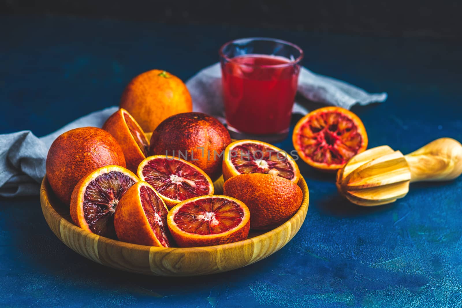 Shorts of alcohol cocktail with Sliced Sicilian Blood oranges and fresh red orange juice, served on dark blue concrete table surface. Dark rustic style.