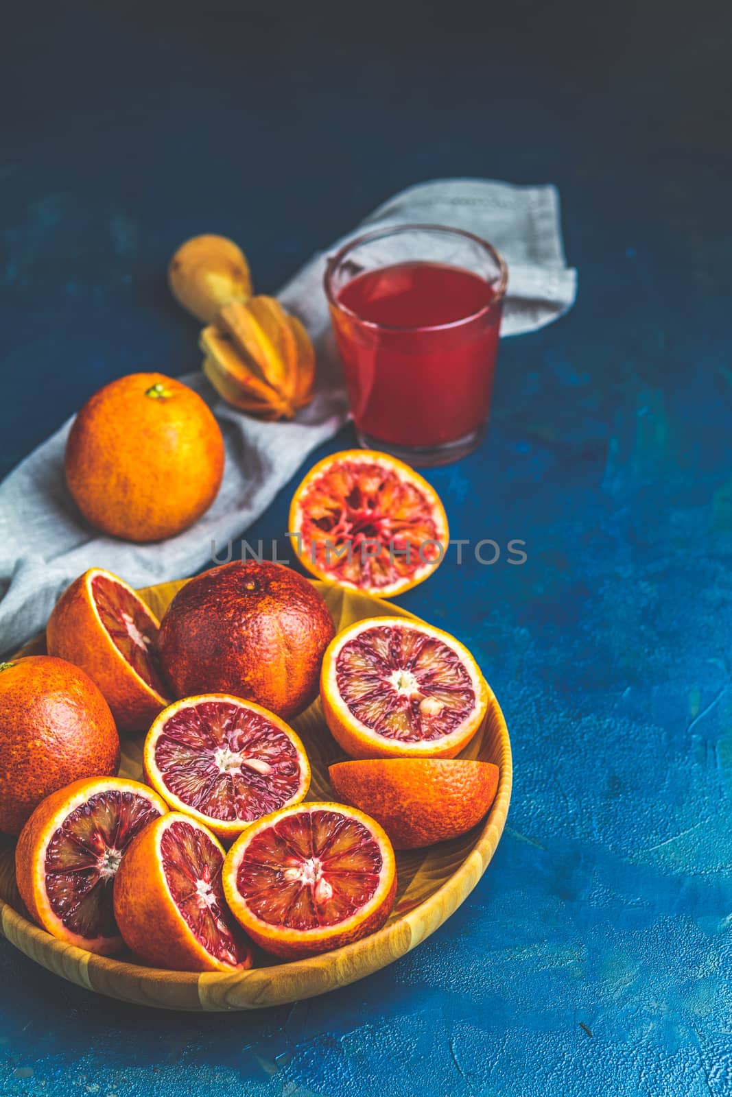 Shorts of alcohol cocktail with Sliced Sicilian Blood oranges and fresh red orange juice, served on dark blue concrete table surface. Dark rustic style.