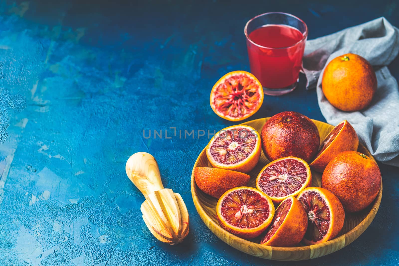 Shorts of alcohol cocktail with Sliced Sicilian Blood oranges and fresh red orange juice, served on dark blue concrete table surface. Dark rustic style.