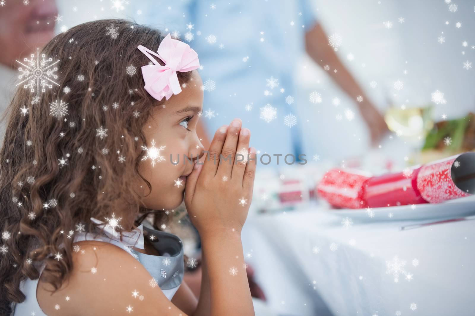 Composite image of Little girl sitting praying at table against snow falling