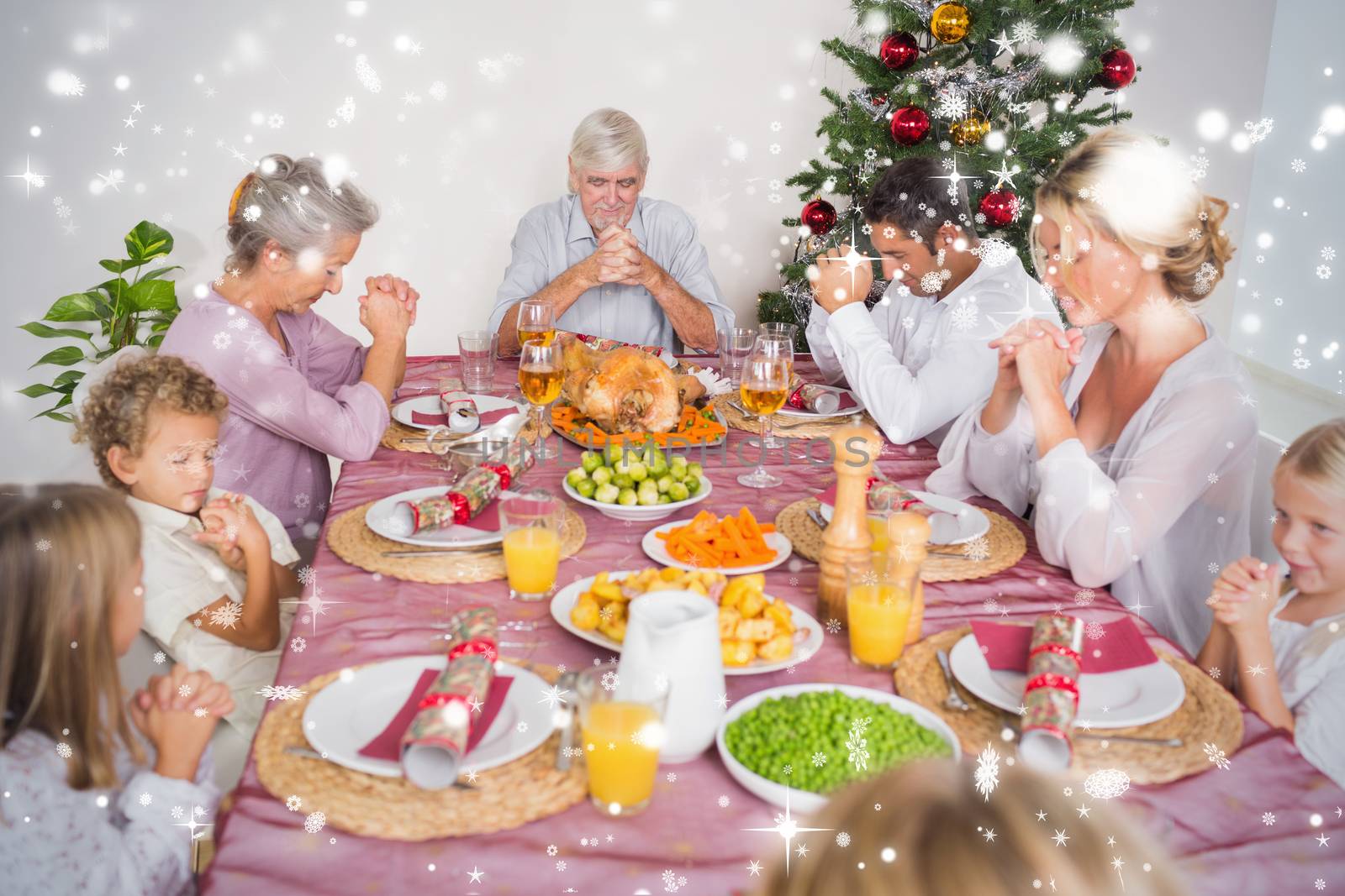Composite image of Family saying grace before christmas dinner against snow falling