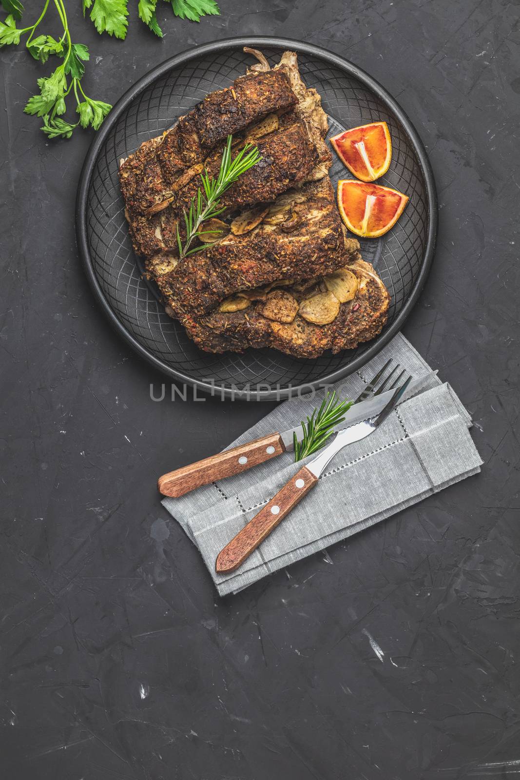 Delicious baked roast pork meat in black ceramic plate with garlic and spices. Dish for dinner. Top view, flat lay, dark concrete surface, copy space for you text