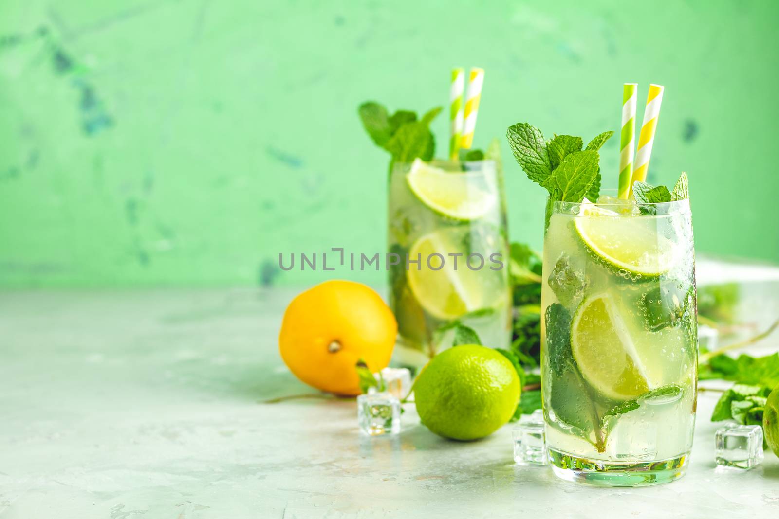 Two mojito cocktails with lime and mint in highball glasses on a gray and green concrete stone surface background. With copy space for your text