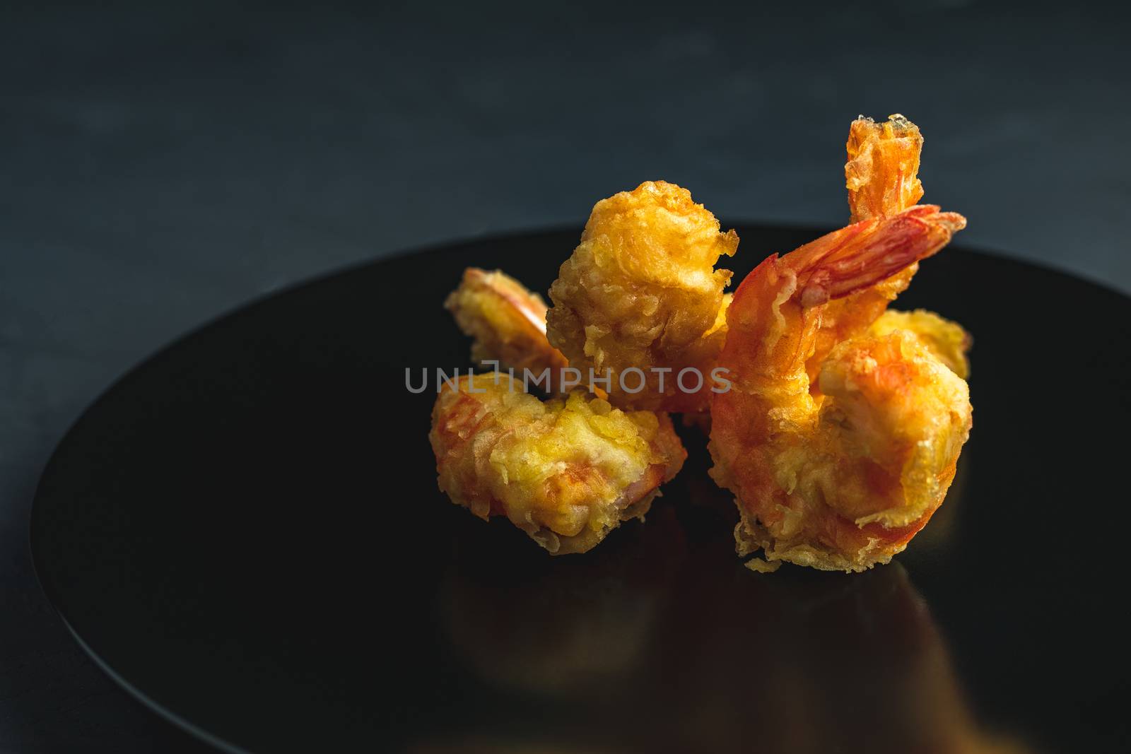 Fried Shrimps tempura in black plate on dark concrete surface background. Copy space for you text. Seafood tempura dish served japanese or eastern Asia style with chopsticks.