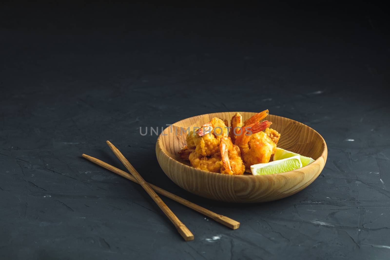 Fried Shrimps tempura with lime in wooden plate on dark concrete surface background. Copy space for you text. Seafood tempura dish served japanese or eastern Asia style with chopsticks.
