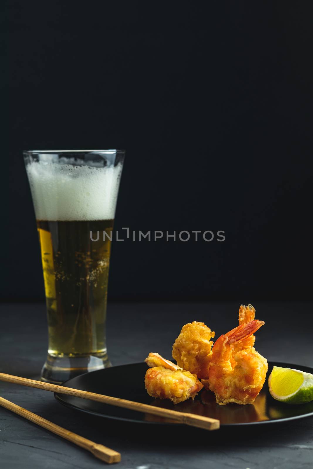 Shrimps tempura with lime in black plate and glass of light beer by ArtSvitlyna