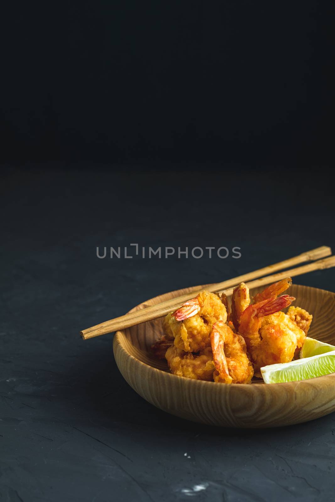 Fried Shrimps tempura with lime in wooden plate on dark concrete surface background. Copy space for you text. Seafood tempura dish served japanese or eastern Asia style with chopsticks.