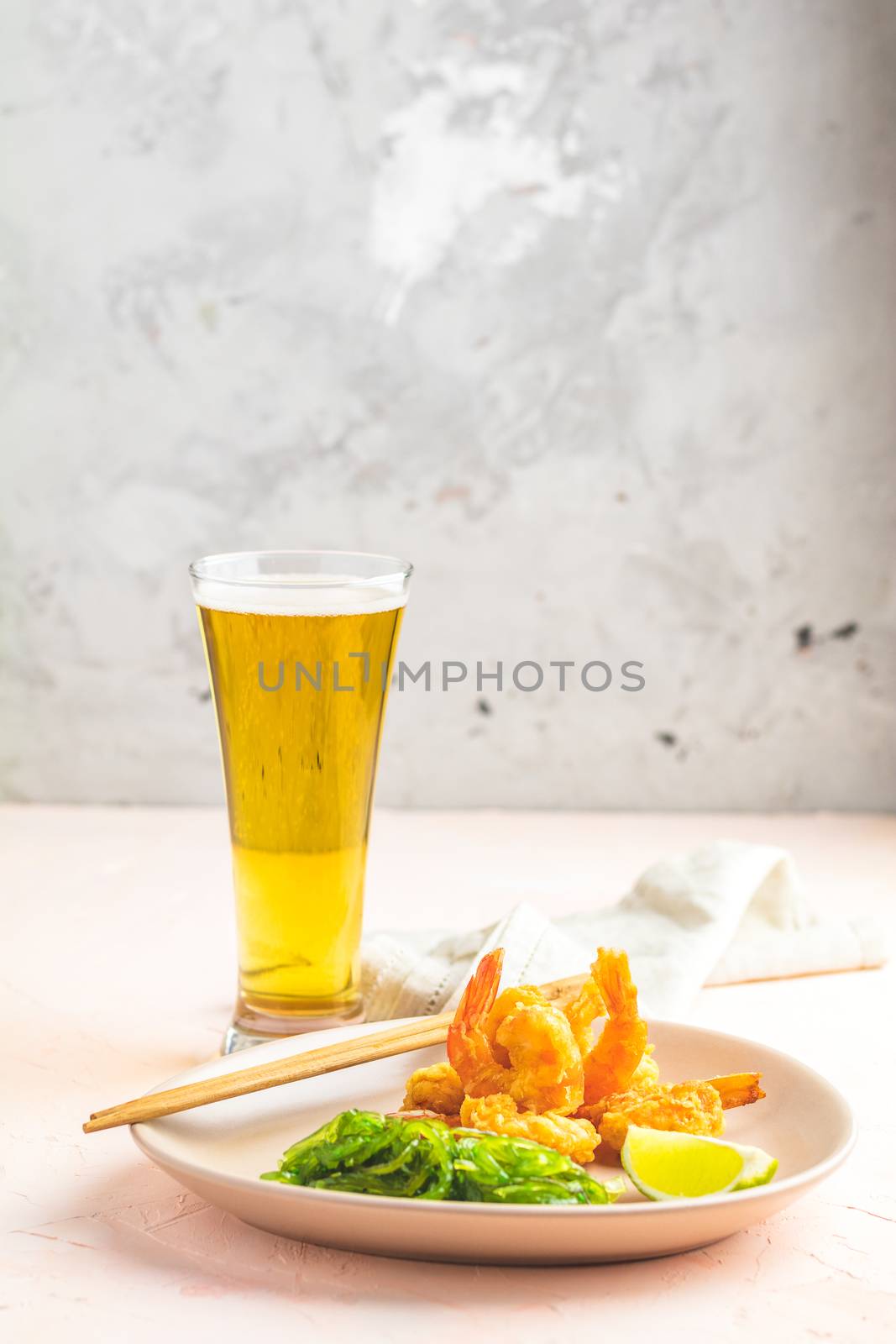 Fried Shrimps tempura with lime in light plate and glass of beer on pink or peach concrete surface background. Copy space Seafood tempura dish served japanese or eastern Asia style with chopsticks