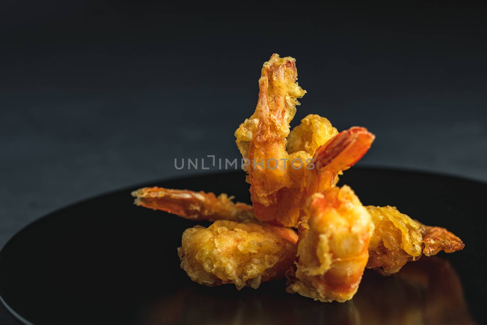 Fried Shrimps tempura in black plate on dark concrete surface background. Copy space for you text. Seafood tempura dish served japanese or eastern Asia style with chopsticks.