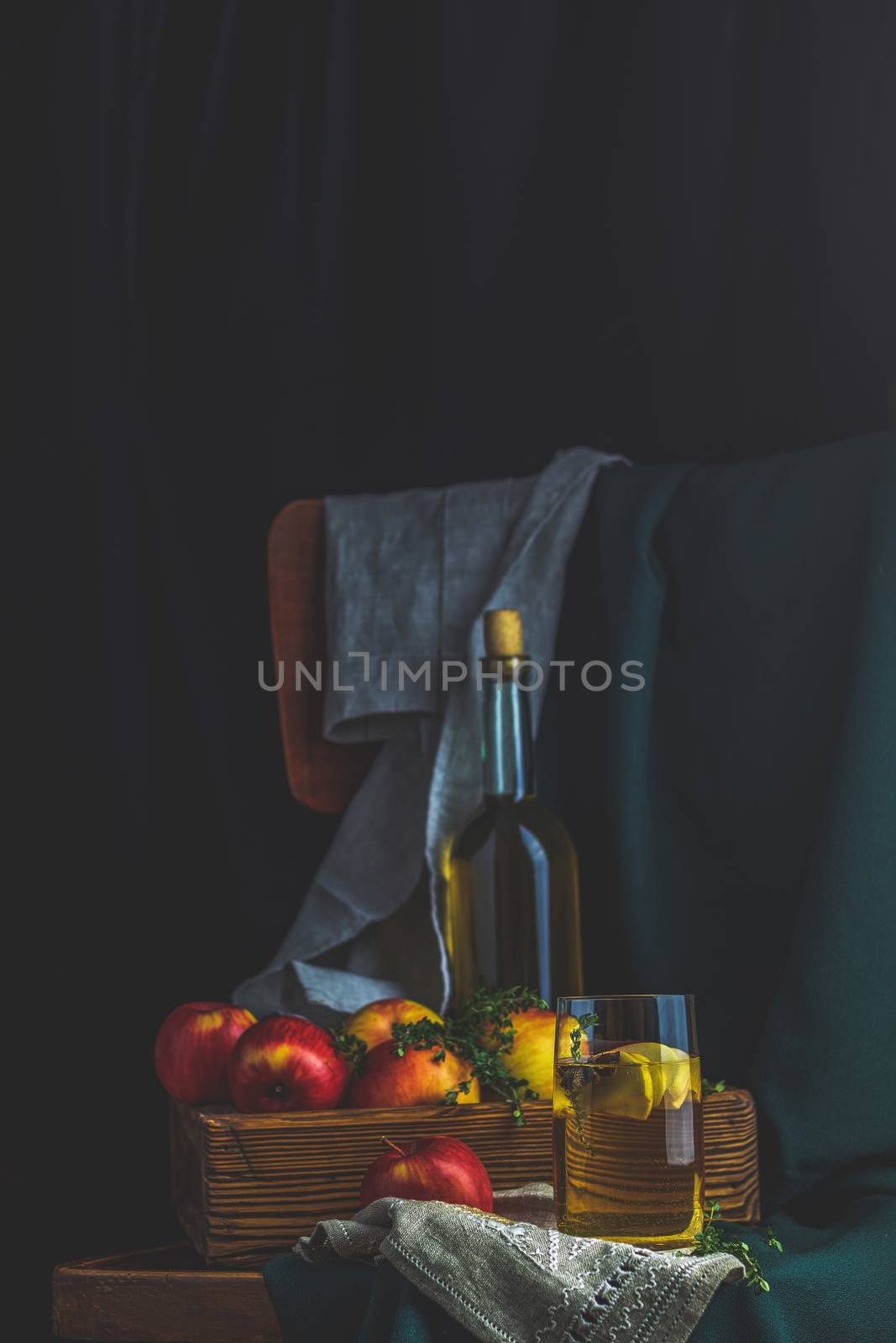 Apple cider vinegar or fruits tea with apple slices in glass with ripe red apples in box, dark vintage rustic style. Shallow depth of the field.