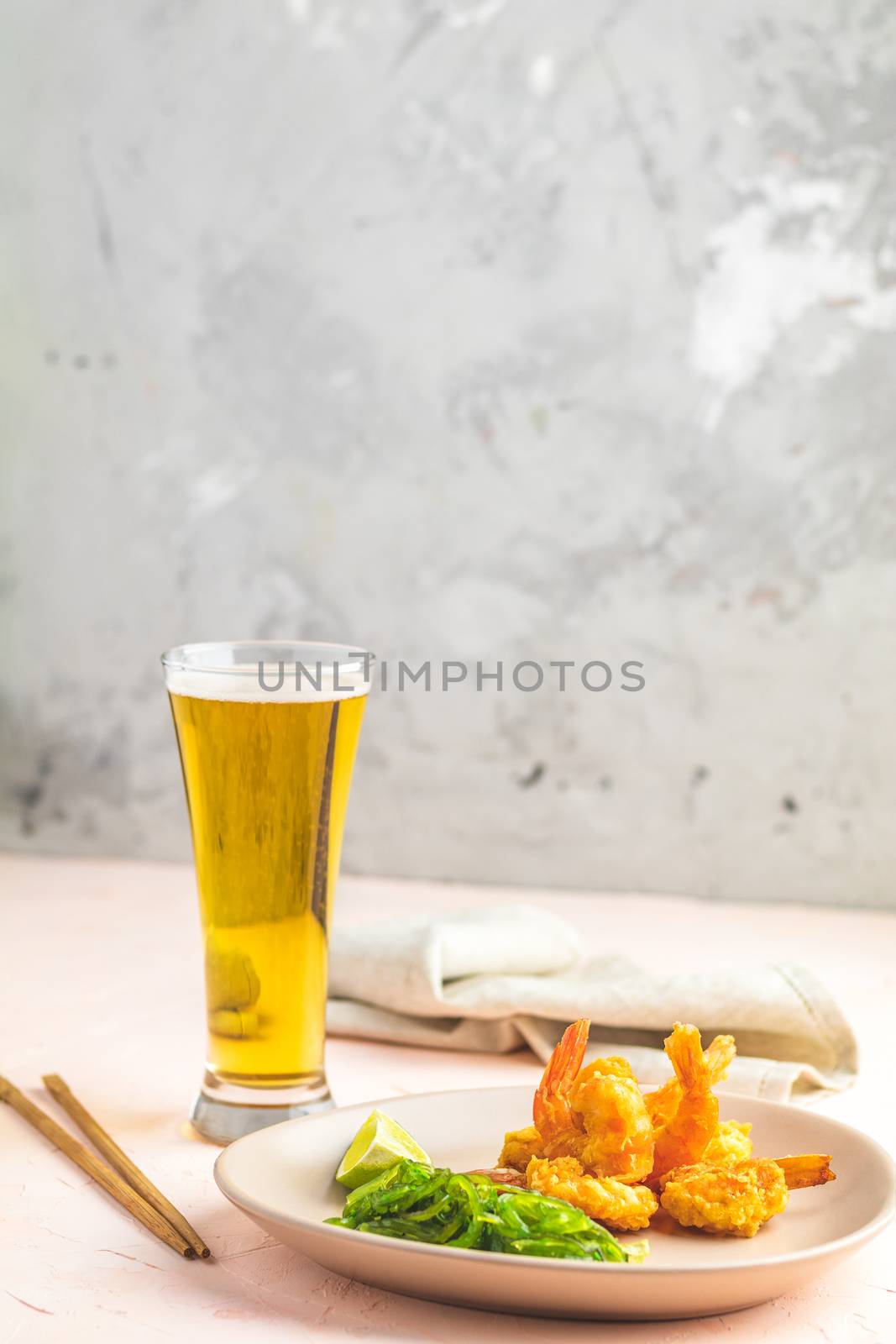 Fried Shrimps tempura with lime in light plate and glass of beer on pink or peach concrete surface background. Copy space Seafood tempura dish served japanese or eastern Asia style with chopsticks
