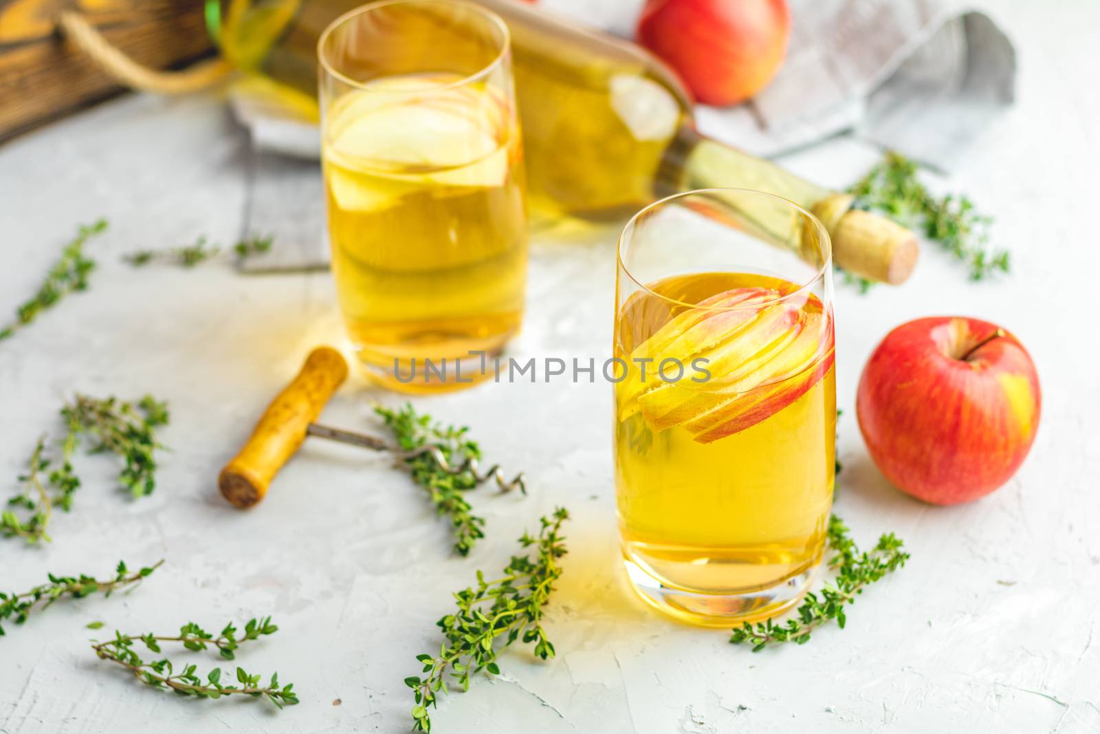 Bottle and glasses of homemade organic apple cider with fresh apples in box, light concrete table surface. Shallow depth of the field.