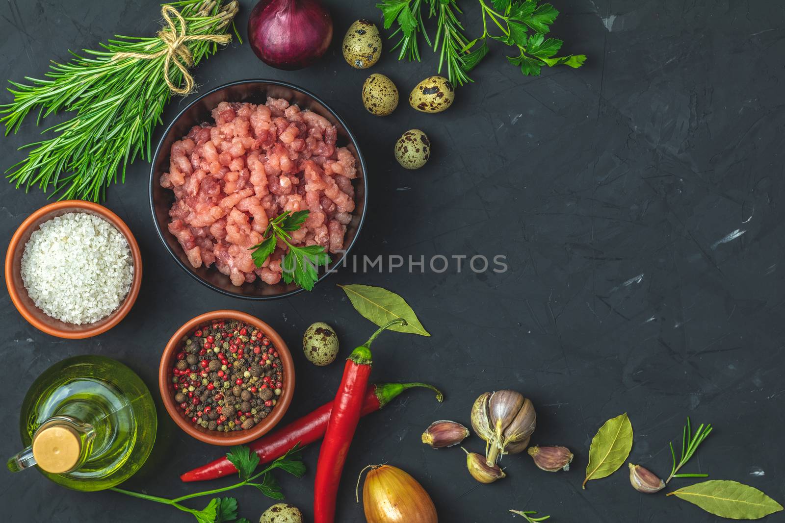 Homemade minced meat in a black bowl over dark slate or stone or concrete background with ingredients for making. Top view with copy space