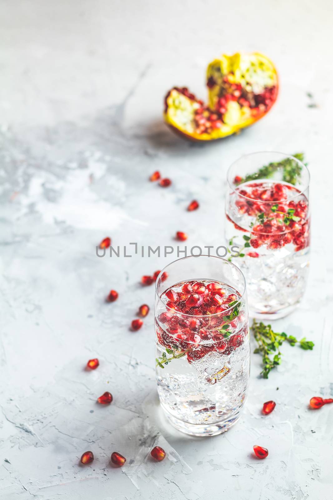 Festive drinks, gin and tonic pomegranate cocktail or detox water with ice. Selective focus, copy space for text, light gray concrete table surface.
