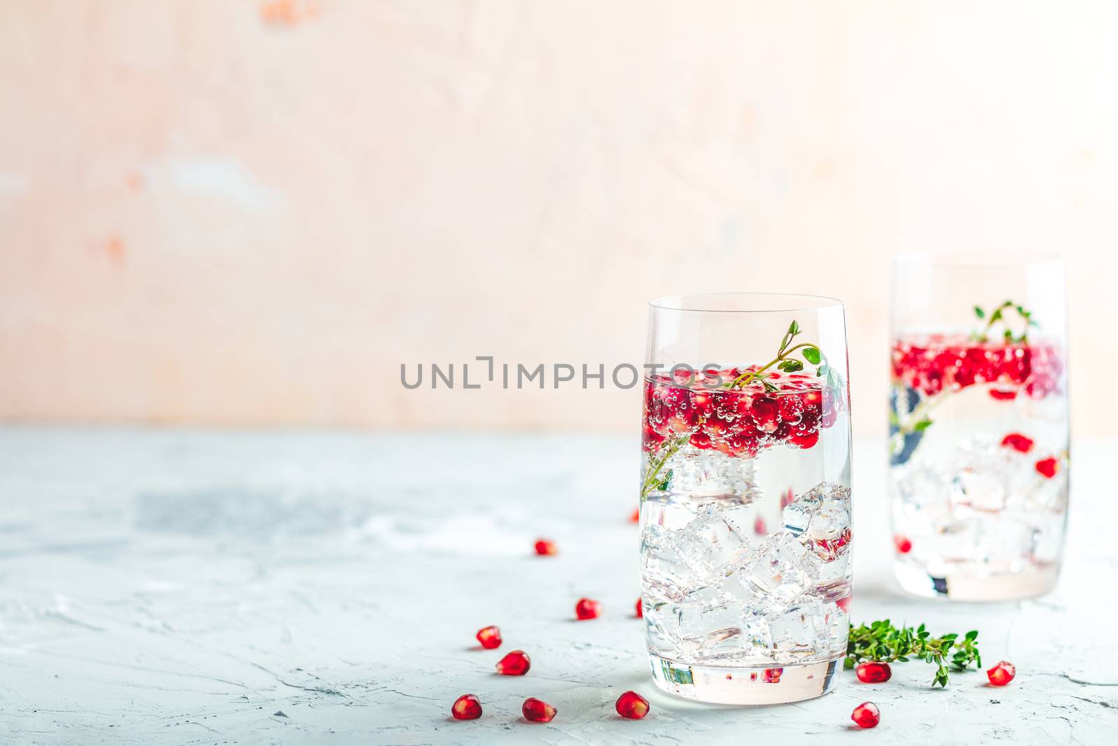 Festive drinks, gin and tonic pomegranate cocktail or detox water with ice. Selective focus, copy space for text, light gray concrete table surface.
