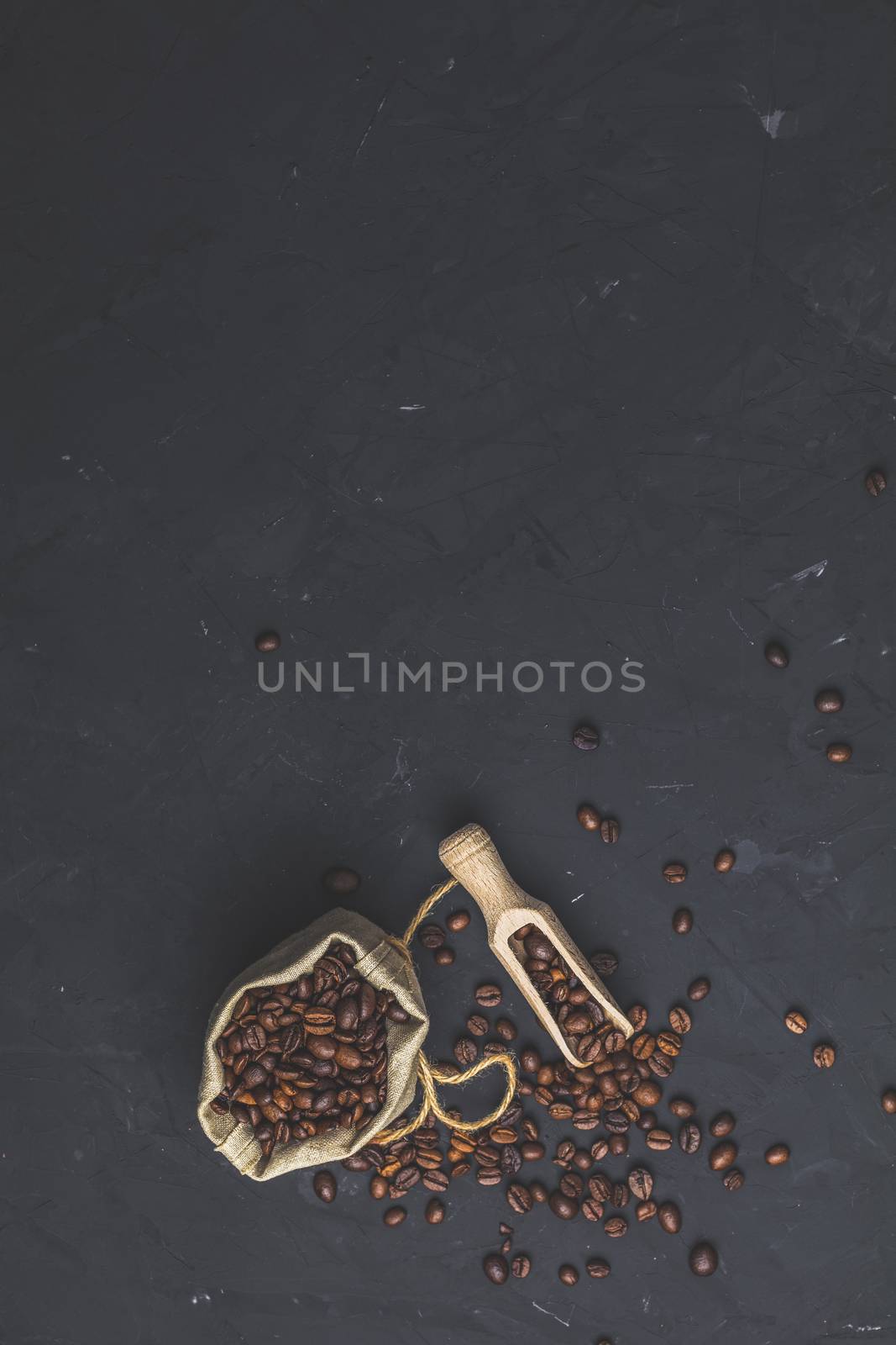 Purse with roasted beans and wooden scoop on black stone concrete textured surface background. Top view with copy space for your text.