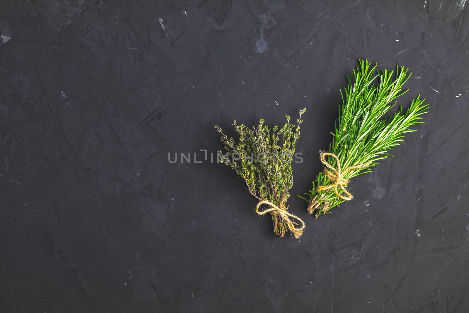 Rosemary and thyme bunches of bouquets on black stone concrete textured surface background. Top view with copy space for your text.