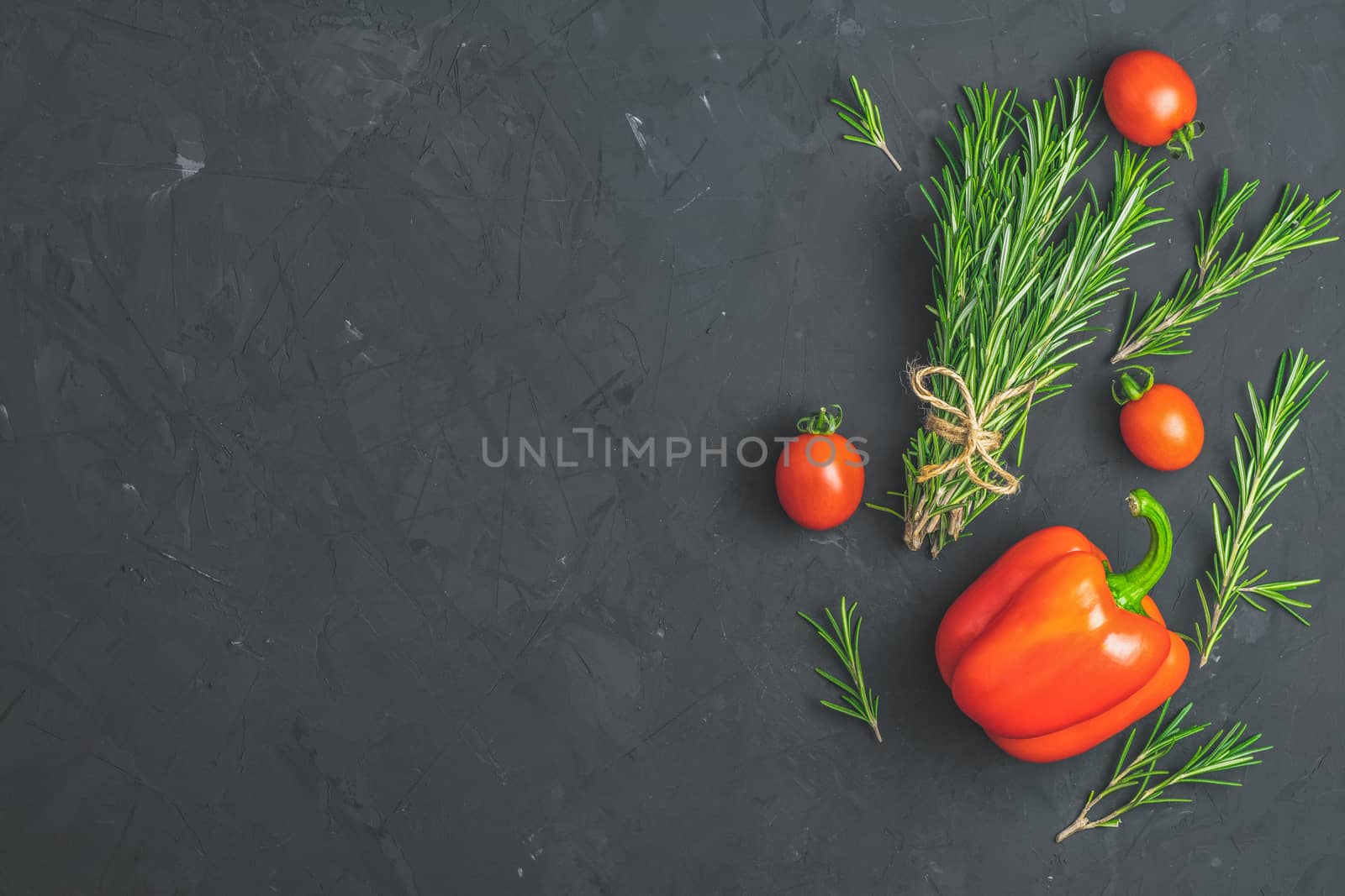 Rosemary bunch of bouquets, raw pepper and cherry tomatoes on black stone concrete textured surface background. Top view with copy space for your text.
